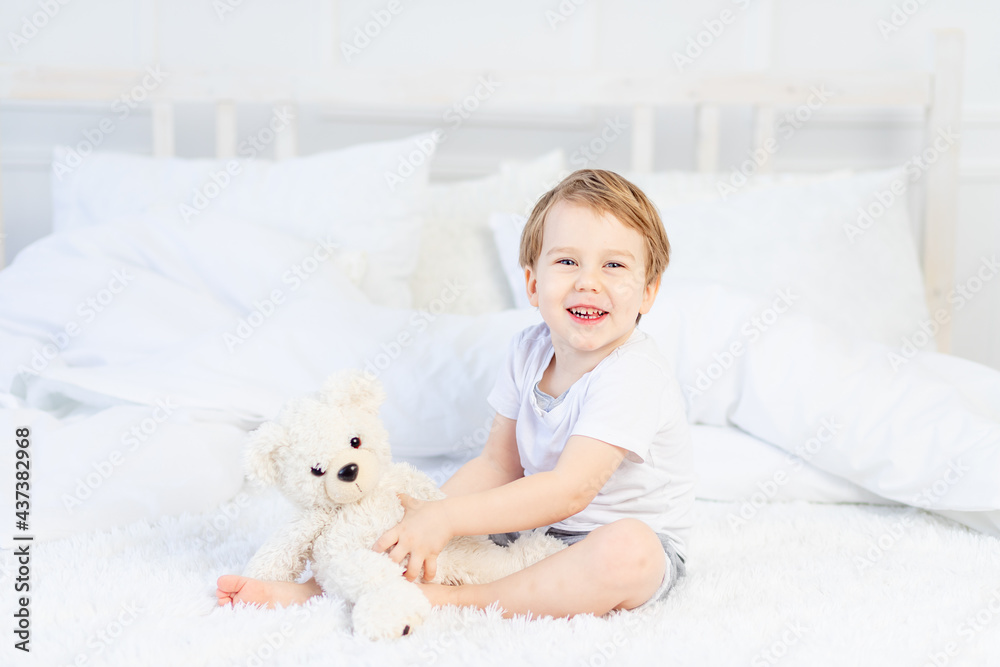 a child with a teddy bear on the bed at home plays and laughs a child with a teddy bear on the bed at home plays and laughs