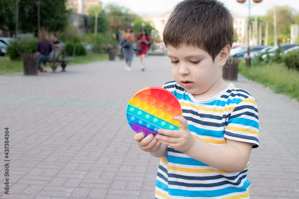 Fototapeta premium A child of 4 years plays with Pop It in the city park. Anti-stress toy for the development of fine motor skills in children.