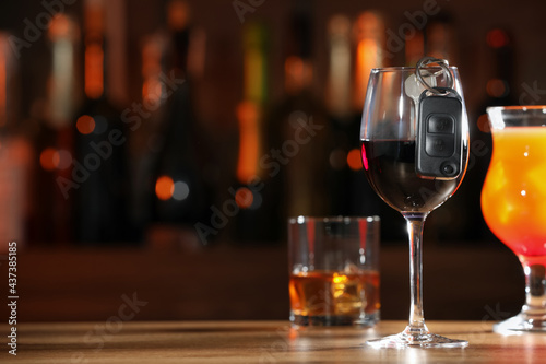 Car key and glass of alcoholic drink on table against blurred background, space for text. Drunk driving concept