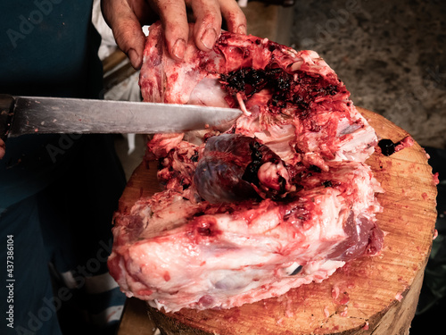 Worker with a large knife slicing the head of a pig on a large wooden log, on a slaughter day. Open pig head seizing meat photo