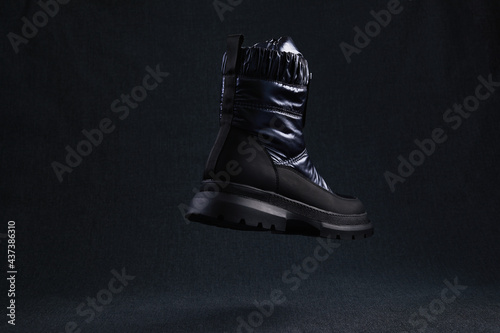 Fashion black unbranded boot flying on dark background. Black winter walking shoes levitate in air. Modern stylish female shoes for off-road walking.