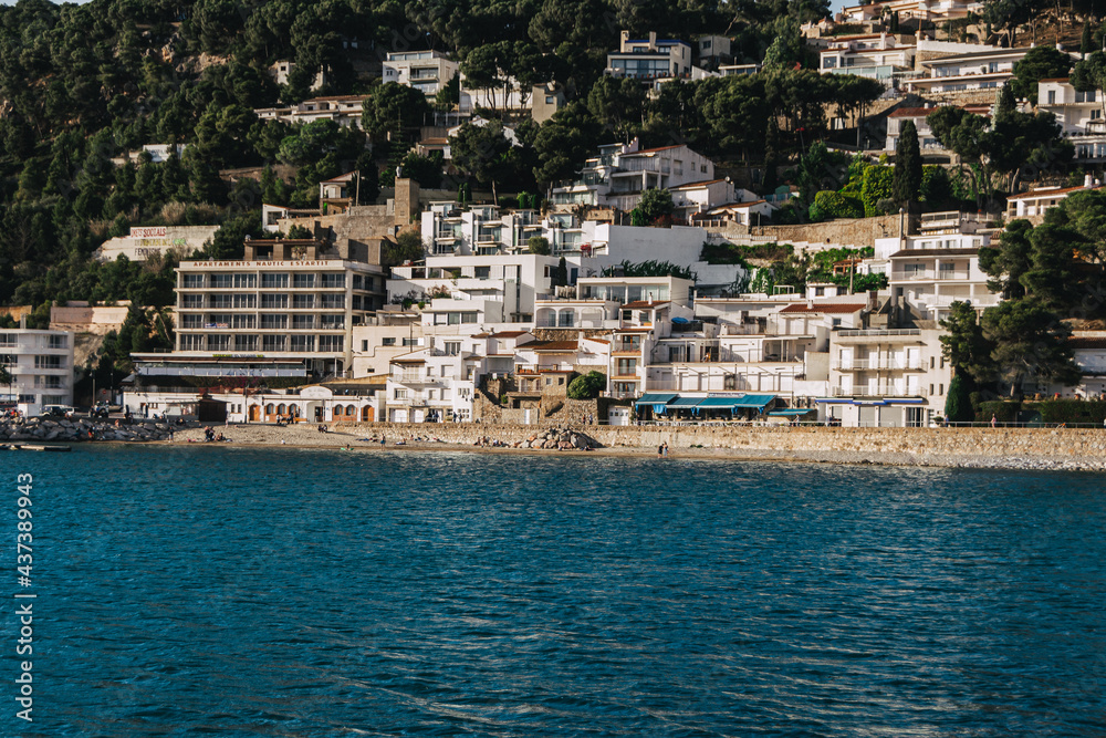 Landscape of l'Estartit, a coastal town on the Costa Brava, white houses in front of the calm and blue sea, people on the beach and lonely sea