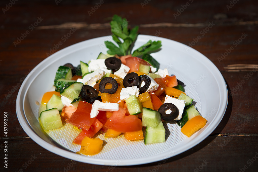 Fresh Greek salad in a disposable dish on a wooden table.