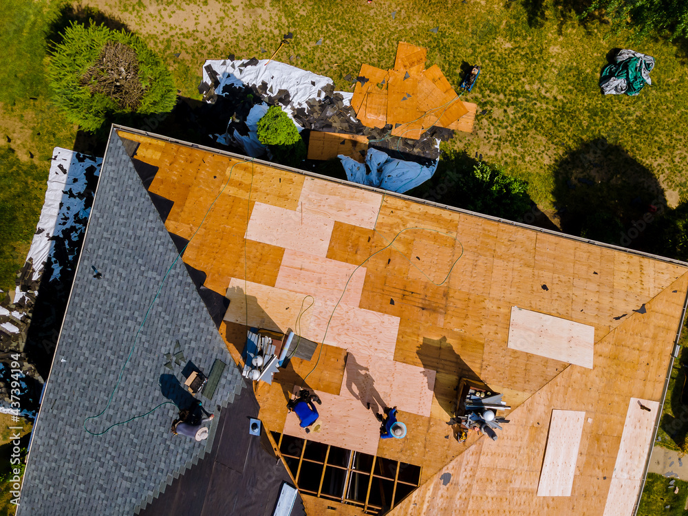Roof construction repairman on a residential apartment with new roof shingle being applied - obrazy, fototapety, plakaty 