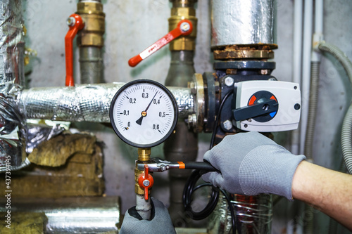 Repair of equipment in an industrial boiler room.  A plumber with a wrench and wearing work gloves corrects problems at the connection point of the pressure gauge photo