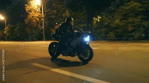 Young man in helmet riding fast on modern black sport motorbike at evening city street. Motorcyclist racing his motorcycle on night empty road. Guy driving bike. Concept of freedom and hobby. Close up