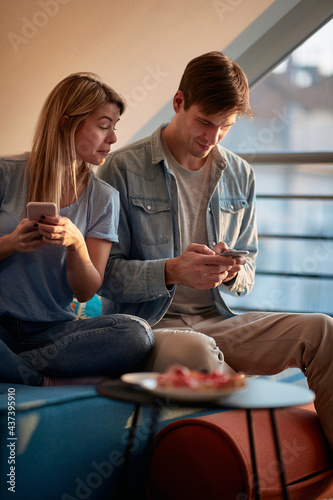 Obraz na plátně A girl is spying her boyfriend's smartphone while sitting on the sofa at home together