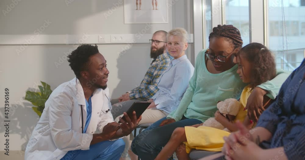 Afro-american male doctor talking to mother and kid in hospital waiting room