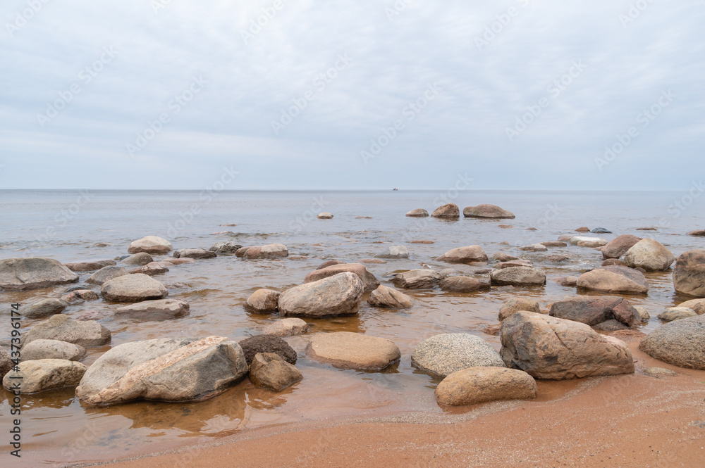 Sandy beach of  Baltic sea covered with big stones in overcast spring morning