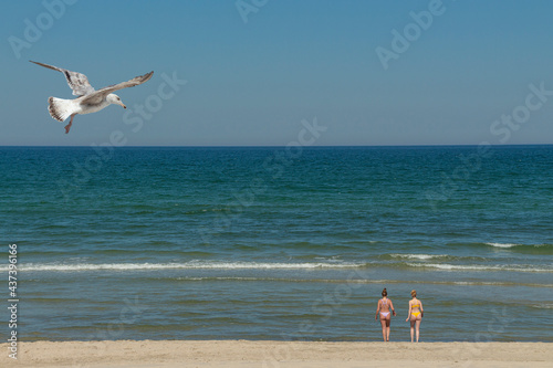 Zwei badende Frauen am Strand, im Urlaub, mit Sand und Meer und Wellen, Himmel und Möwe 