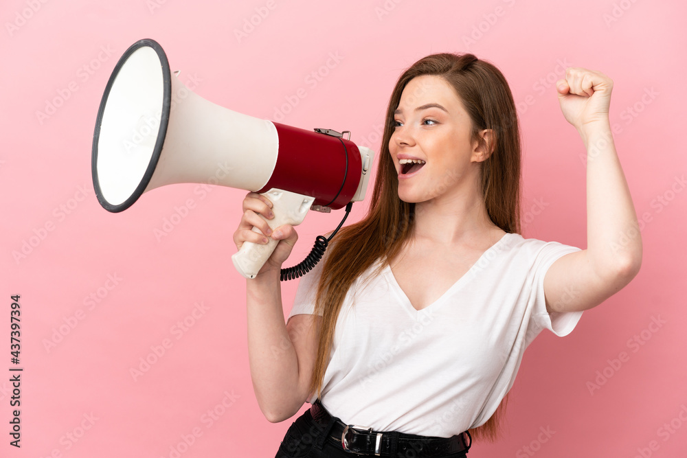 Teenager girl over isolated pink background shouting through a megaphone to announce something in lateral position