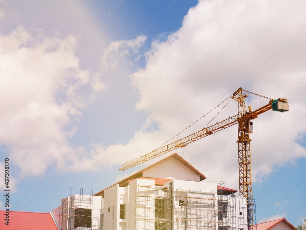 The crane is working on a tall building overlooking the sky and white clouds. The crane is working on a tall building overlooking the sky and white clouds.
