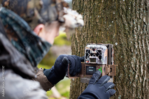 Obraz na płótnie Wildlife enthusiast setting up a trail camera on tree and operating buttons. Nature researcher preparing device to monitor local animals using motions sensors. w salonie