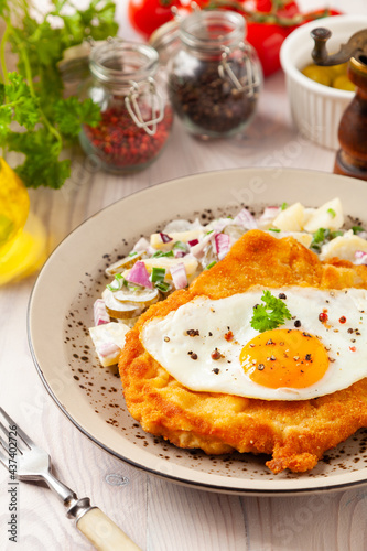 Viennese pork schnitzel with a fried egg. Served on potato salad. Natural wooden planks in the background.