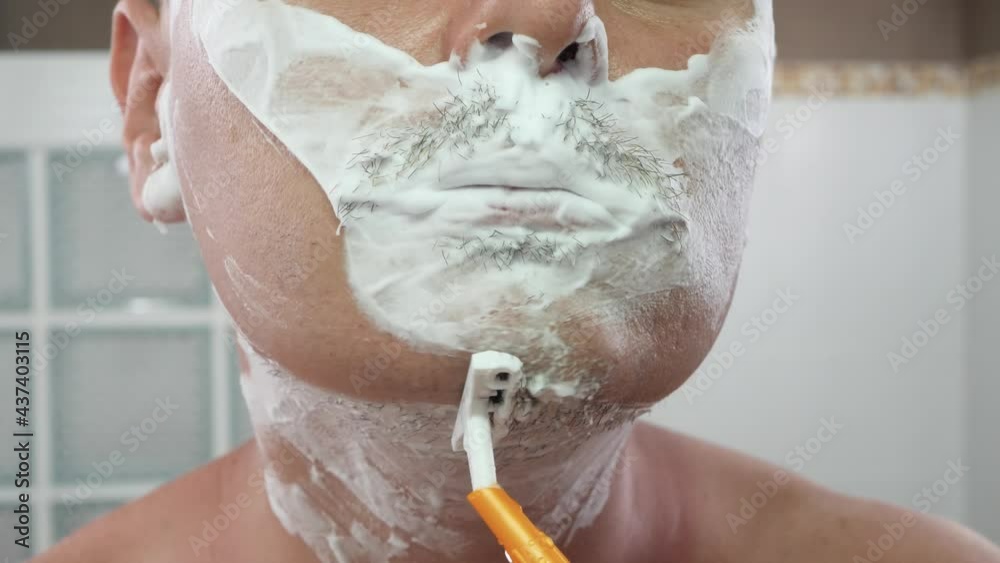 Young adult male shaving by blade razor. Real man apply shaving foam on