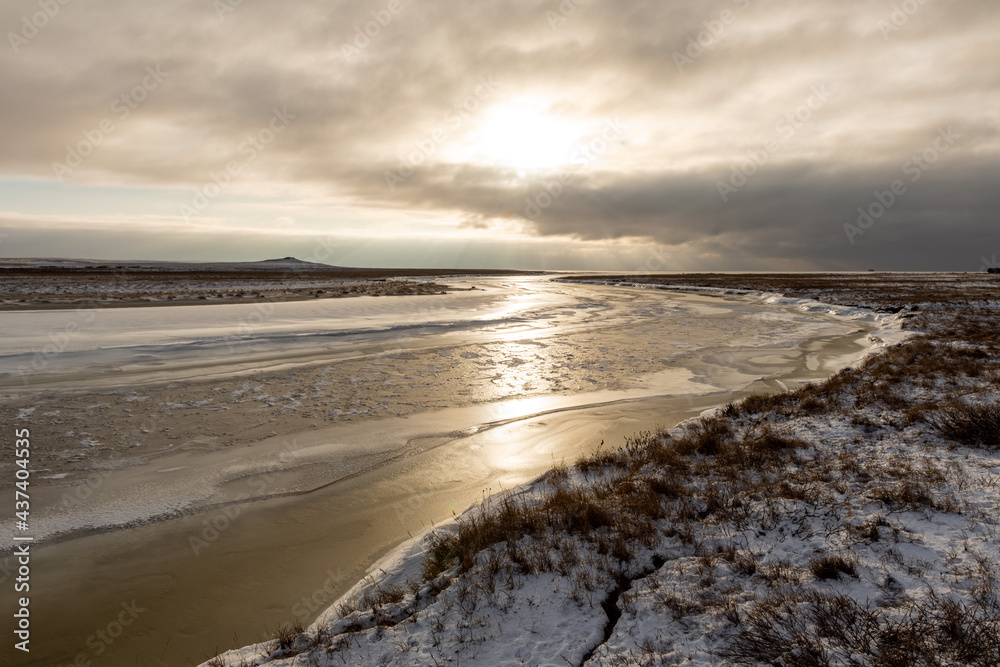 Arctic landscape in winter time. Small river with ice in tundra.