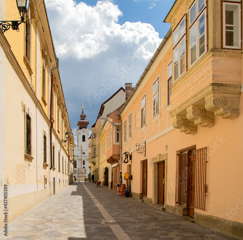 Charming cobbled street with baroque houses towards Szechenyi square in Gyor  Hungary. At the end of the street you can see the Benedictine church and the St.Mary s column.