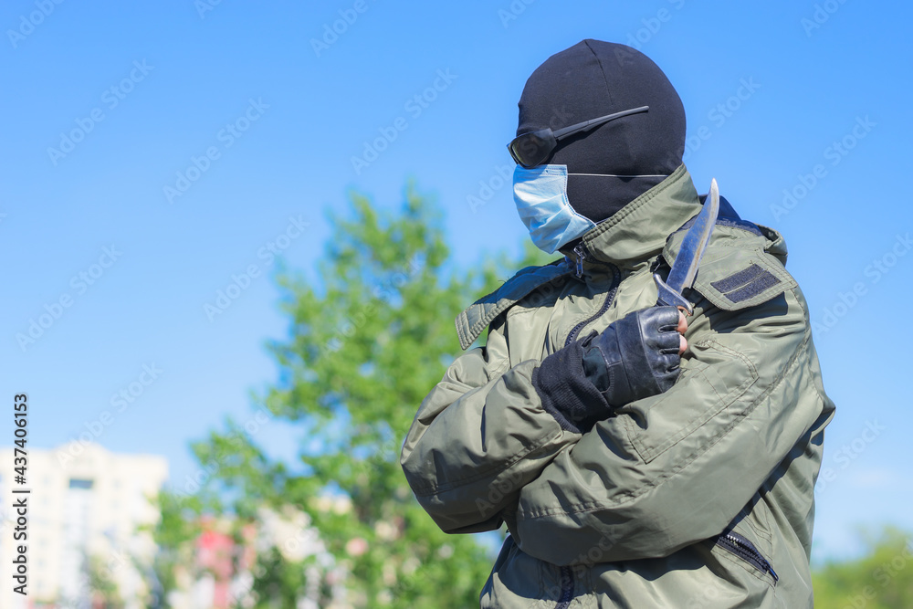 Modern dangerous and armed criminal in balaclava and medical mask among city streets
