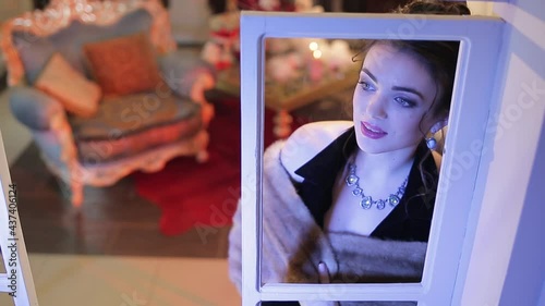 The atmosphere of waiting for Christmas. A young, beautiful woman looks out the window to the street.