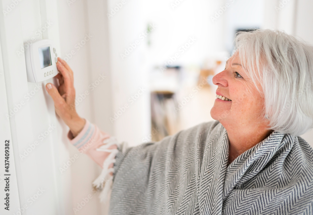 Senior woman adjusting her thermostat at home Senior woman adjusting her thermostat at home