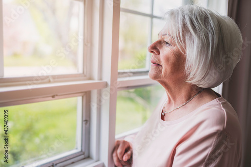 Middle aged female in front of curtains close to a window feel lonely