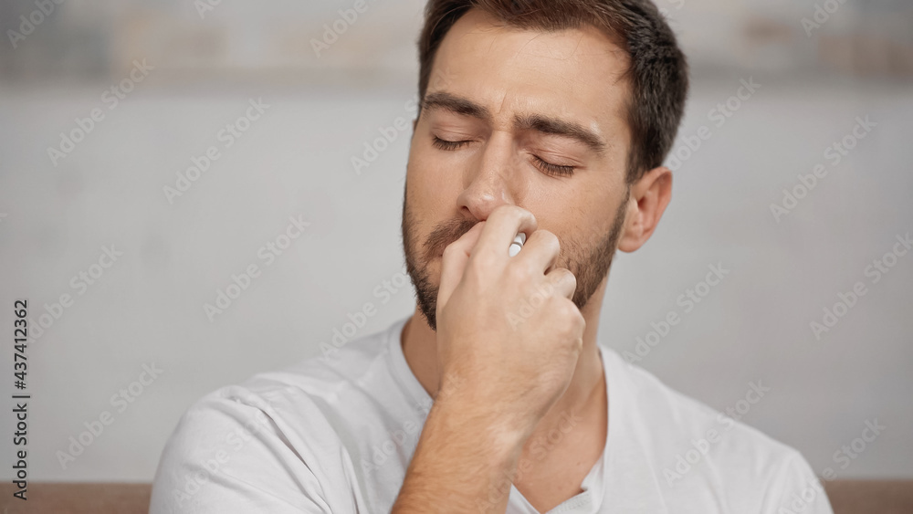 allergic man in white t-shirt using nasal spray at home allergic man in white t-shirt using nasal spray at home