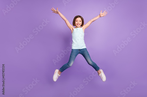 Full body photo of active brown hairdo small girl jump wear blue top jeans isolated on violet color background © deagreez
