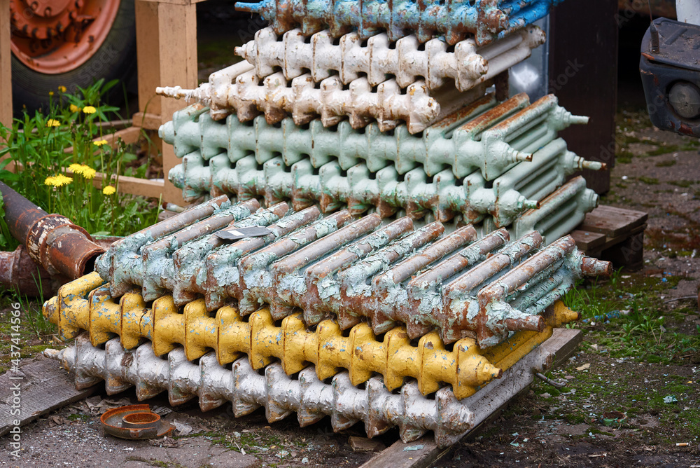 Multi colored cast iron radiators, old heating elements stacked in heap. Old batteries made of cast iron lying on the ground