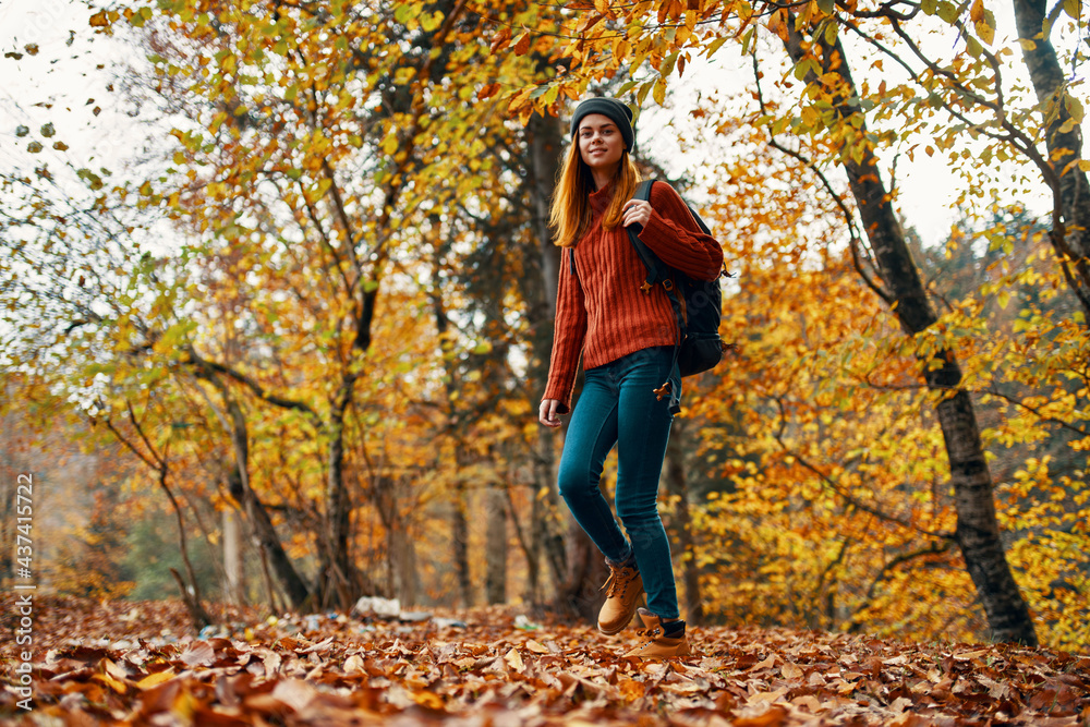 young woman in jeans and a sweater with a backpack on her back walks in the park in autumn in nature, bottom view