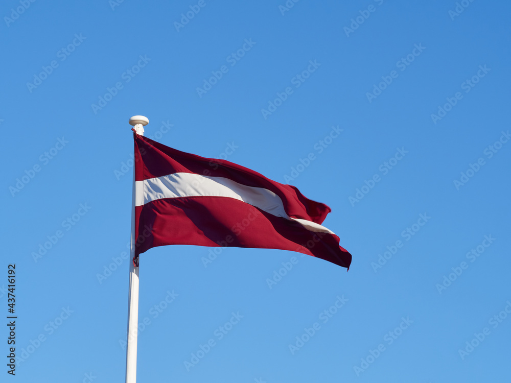 The national flag of Latvia waving in the wind on the flagpole. Horizontal frame.