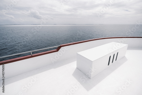 A wide-angle view from the upper deck of a safari yacht with a rectangular box bench with three holes from the ventilation system, lit by the hot summer sun, with a seascape in a defocused background