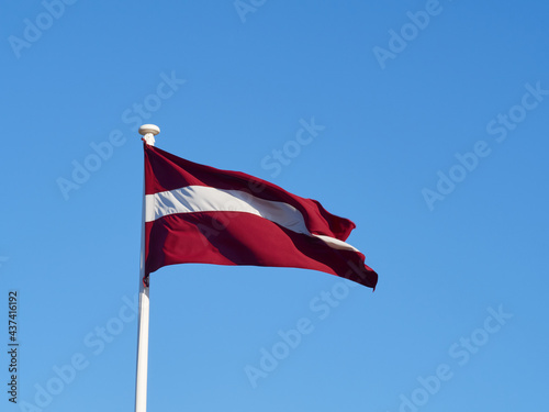 The national flag of Latvia waving in the wind on the flagpole. Horizontal frame.