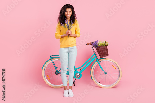 Fototapeta Naklejka Na Ścianę i Meble -  Full length body size view of pretty cheerful girl with bike holding fresh flowers isolated over pastel pink color background