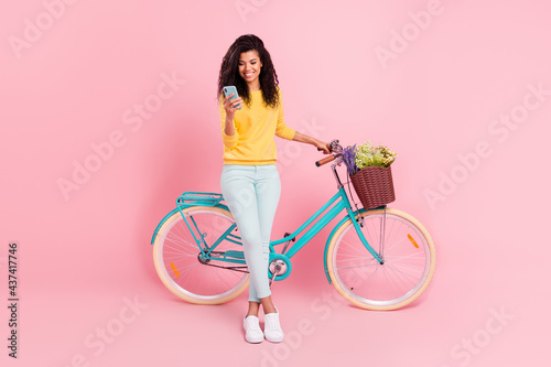 Full length body size view of pretty cheerful girl with bike using device blogging chatting isolated over pastel pink color background © deagreez