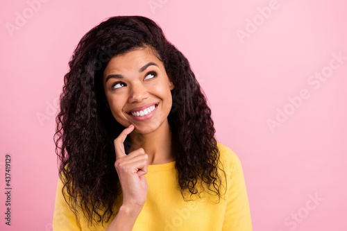 Photo of young cheerful black girl curious look empty space touch finger chin isolated over pink color background