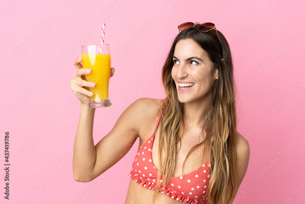 Young blonde woman over isolated pink background in swimsuit and holding a cocktail Young blonde woman over isolated pink background in swimsuit and holding a cocktail