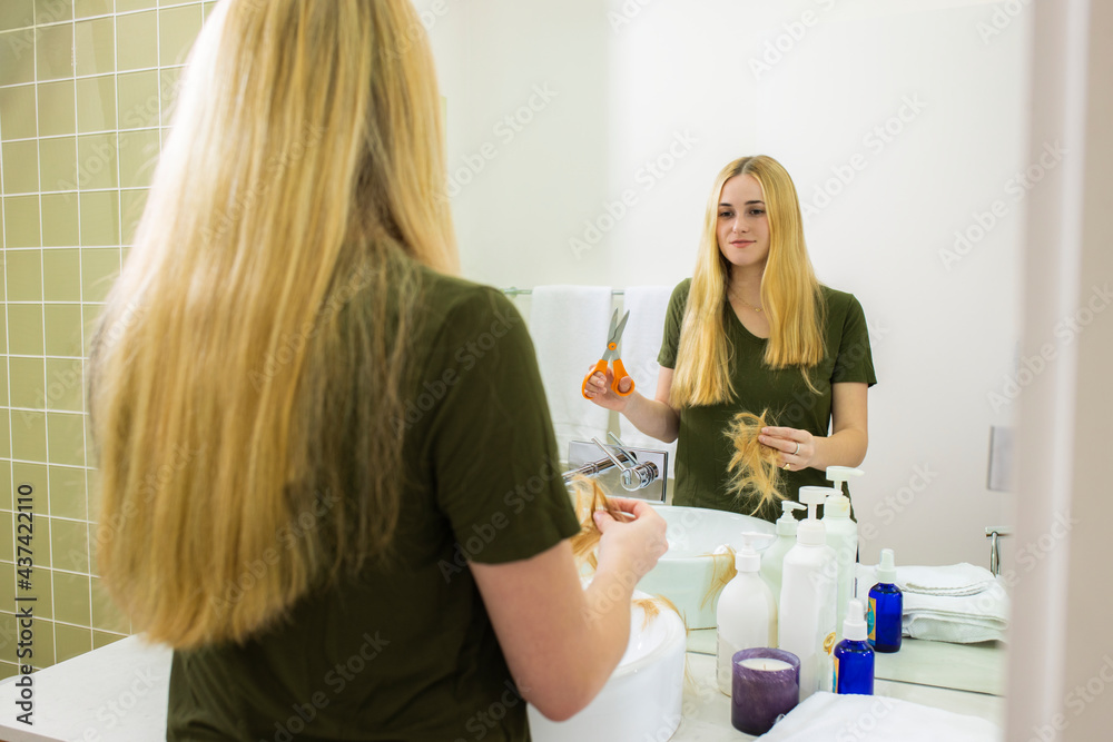 Young woman in home bathroom looking in mirror after cutting her own hair with scissors Young woman in home bathroom looking in mirror after cutting her own hair with scissors