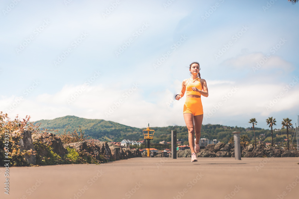 Young woman doing sports wearing an orange sports kit at the park of Hendaia, Basque County. Young woman doing sports wearing an orange sports kit at the park of Hendaia, Basque County.
