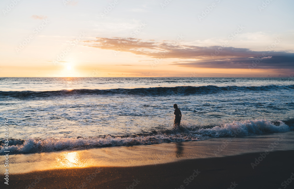 Silhouette of person walking into waving ocean