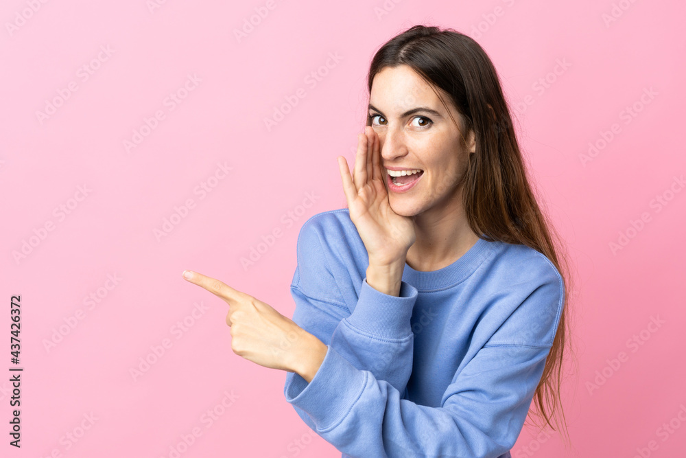 Young caucasian woman isolated on pink background pointing to the side to present a product and whispering something Young caucasian woman isolated on pink background pointing to the side to present a product and whispering something