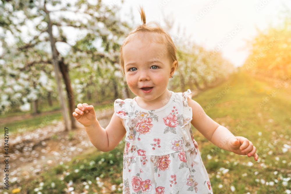 Adorable little smiling baby girl playing in a blooming apple garden Adorable little smiling baby girl playing in a blooming apple garden