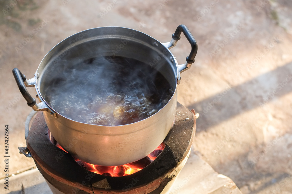 Cooking pork stew in a pot stainless steel is boiling and smoke on a charcoal stove close up. Cooking pork stew in a pot stainless steel is boiling and smoke on a charcoal stove close up.