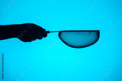 Silhouette of a hand with a metal strainer and a blue background. photo
