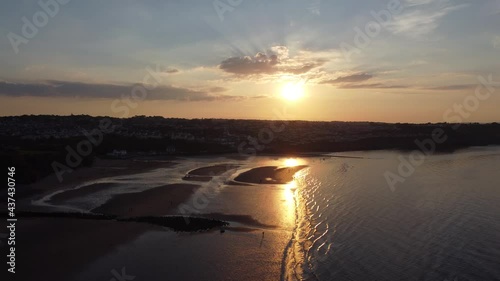 Sunset rays beam fiery golden colours across relaxing beach ocean coastline aerial view slow rising pull back photo