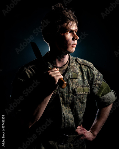 Portrait of soldier with scars and combat coloring, holding a machete in the urns on a black background