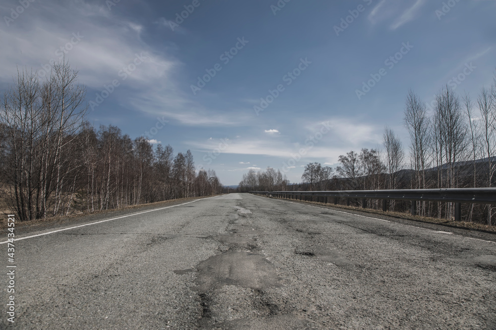 Old road in the forest against the background of the sky. Asphalt road. Beautiful nature.