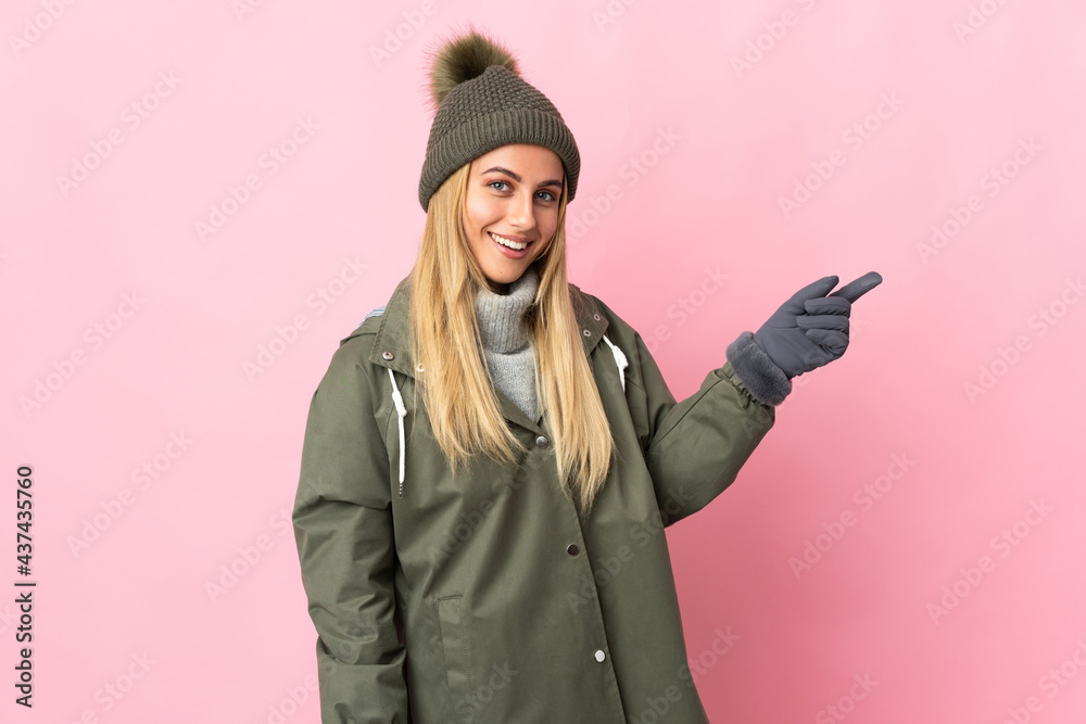 Young woman with winter hat isolated on pink background pointing finger to the side Young woman with winter hat isolated on pink background pointing finger to the side