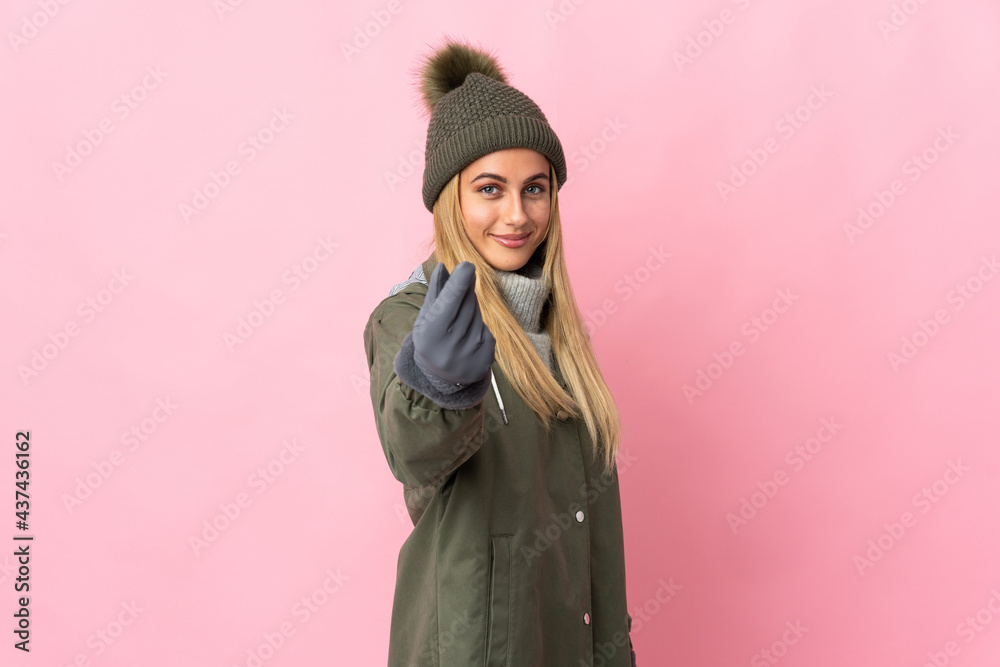 Young woman with winter hat isolated on pink background making money gesture Young woman with winter hat isolated on pink background making money gesture