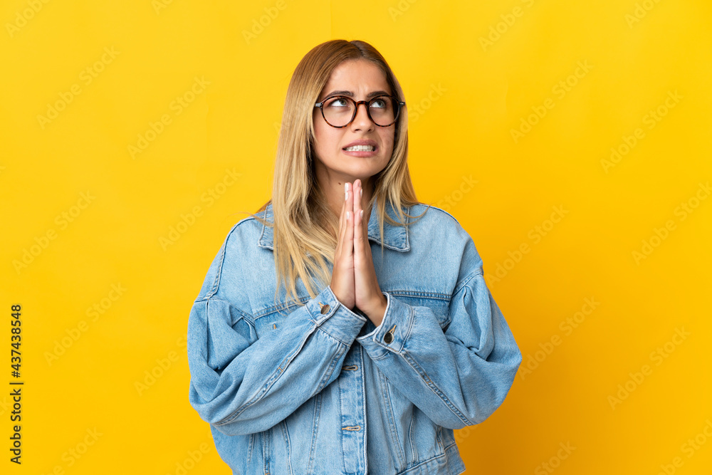 Young blonde woman isolated on yellow background keeps palm together. Person asks for something