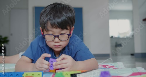 Portrait attractive smart cute happy Asian little kid child boy wearing eyeglasses enjoy playing colorful tower blocks in living room